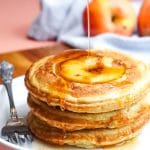 Cinnamon syrup being poured over a stack of apple pancakes.