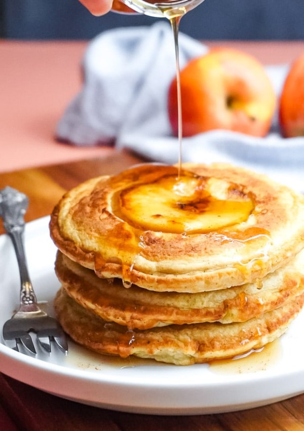 Cinnamon syrup being poured over a stack of apple pancakes.