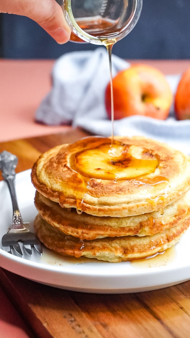 Cinnamon syrup being poured over a stack of apple pancakes. 