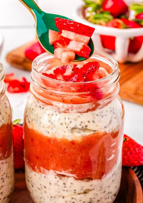 A green spoon adding strawberries to the chia seed parfait.