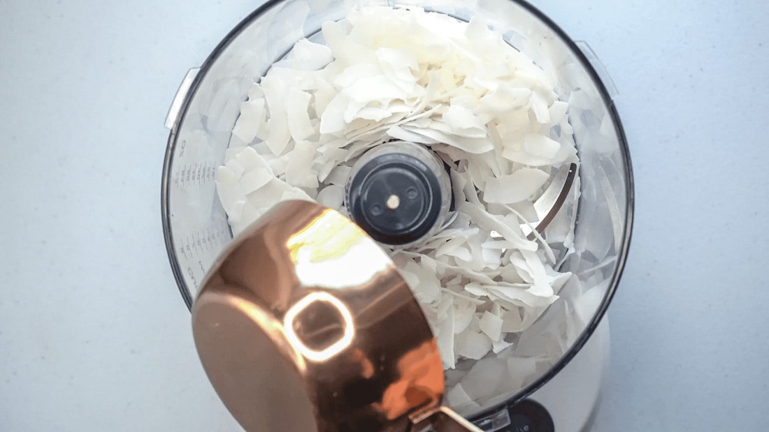 Flaked coconut being poured into a food processor.