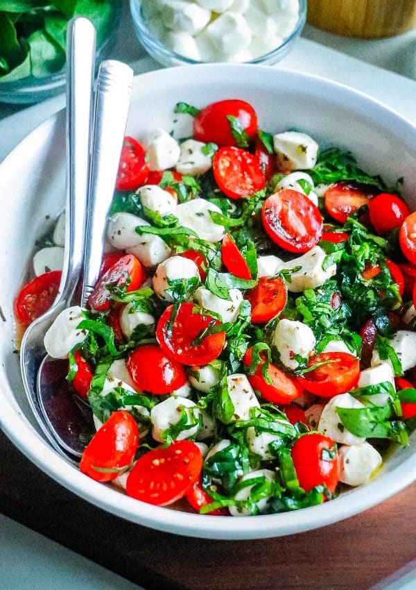 An overhead picture of Spinach Caprese Salad in a white serving bowl with serving spoons.