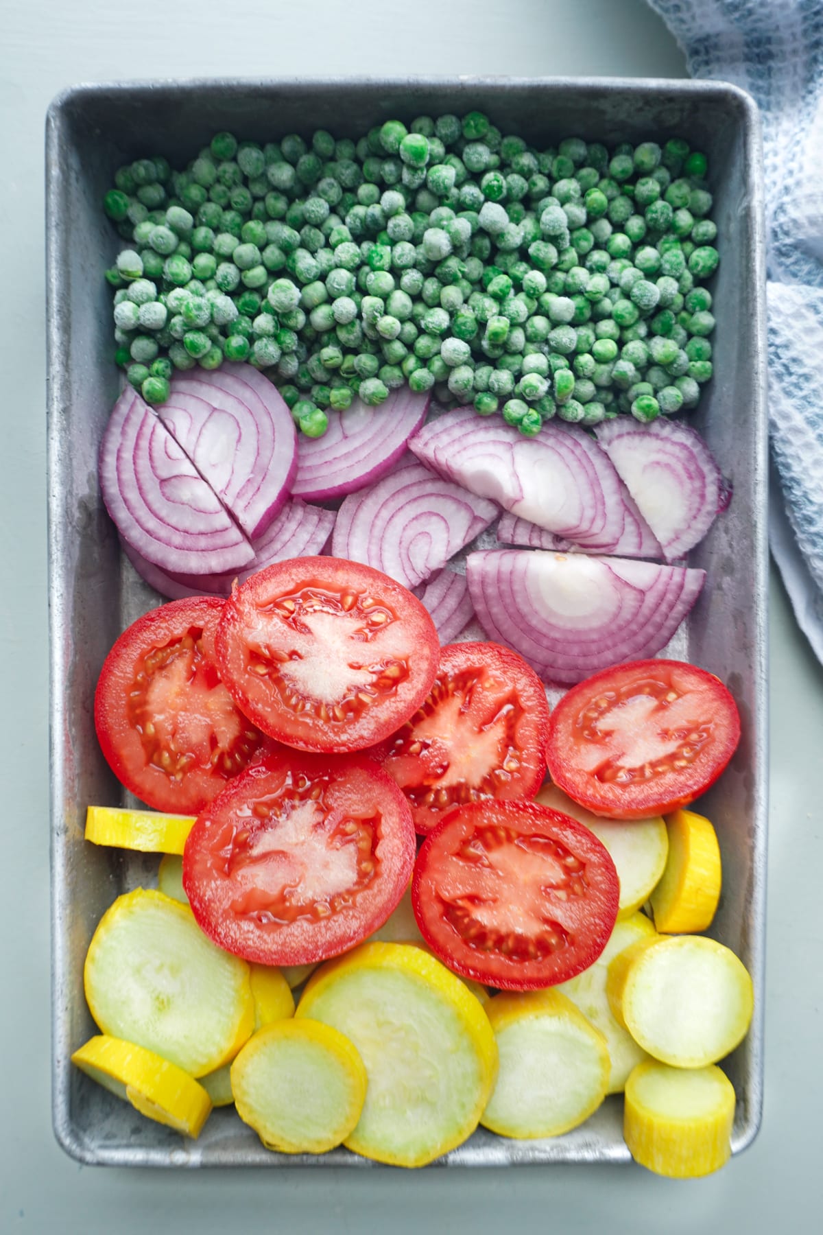 squash, tomatoes, onions, and peas in a baking pan