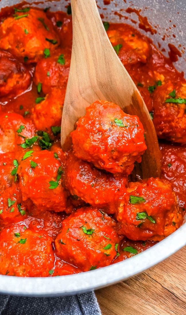 A wooden spoon picking up one of the Ajvar Meatballs.