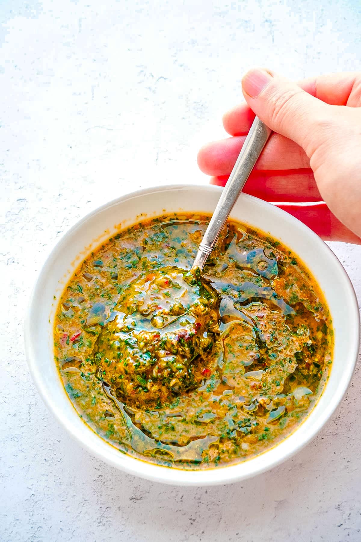 Chimichurri Sauce in a bowl with a spoon being listed from the bowl. 