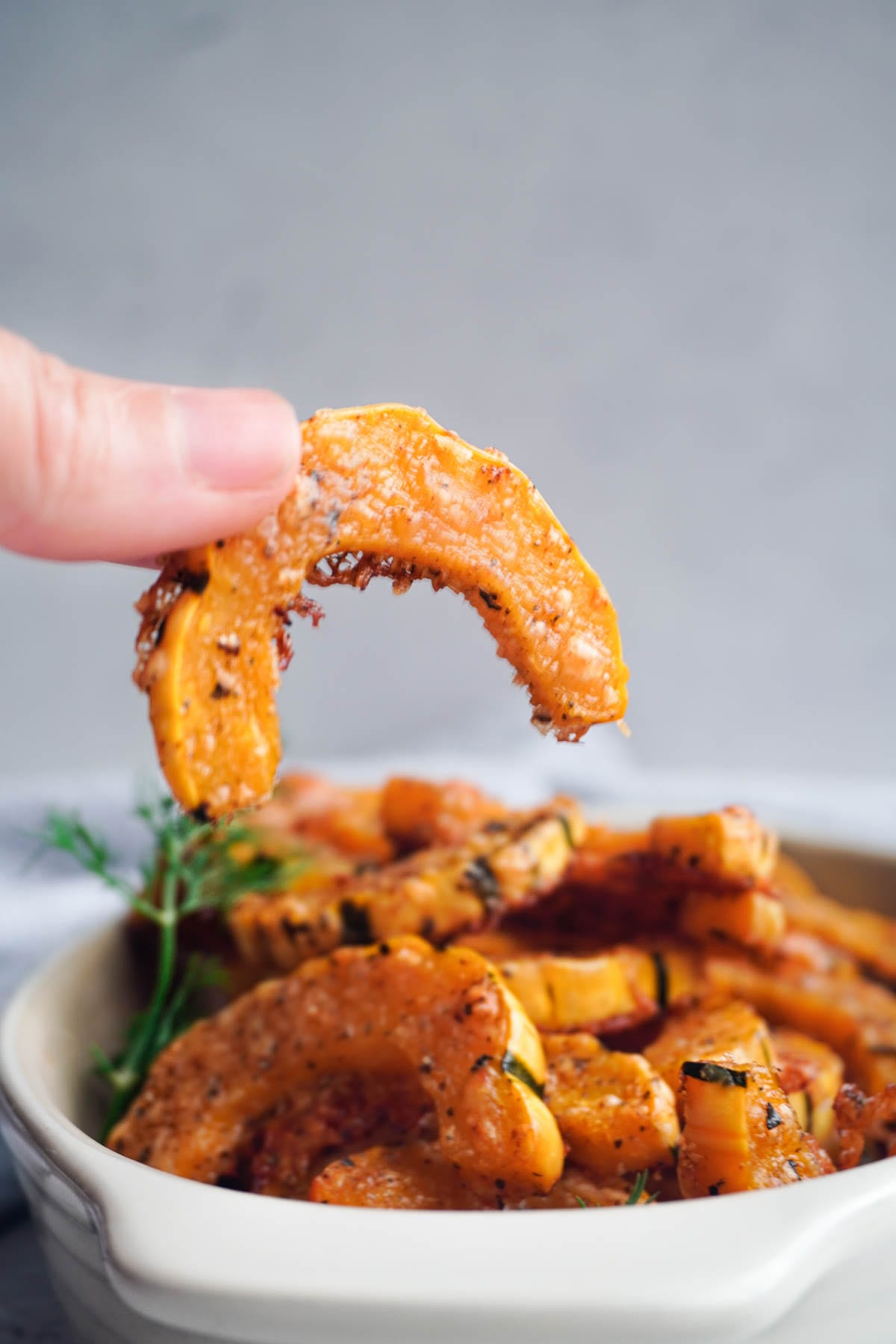 a hand holding up a piece of roasted delicata squash