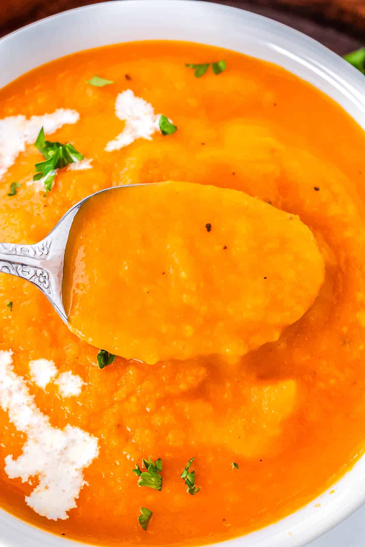 A spoon in a big bowl of carrot and tomato soup.