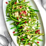 The finished Green Beans that have been sautéed on a white serving platter garnished with sliced almonds and pomegranate seeds.