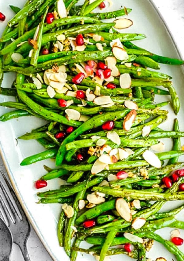 The finished Green Beans that have been sautéed on a white serving platter garnished with sliced almonds and pomegranate seeds.