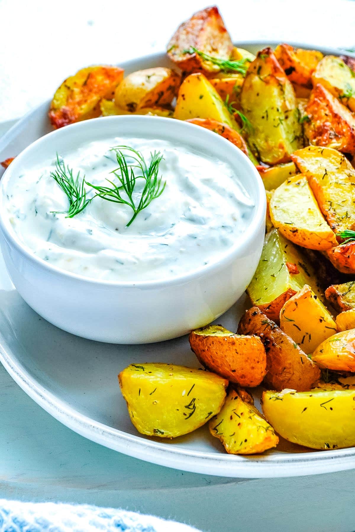 Roasted Potatoes with Dill on a platted with a dish of yogurt dill sauce.