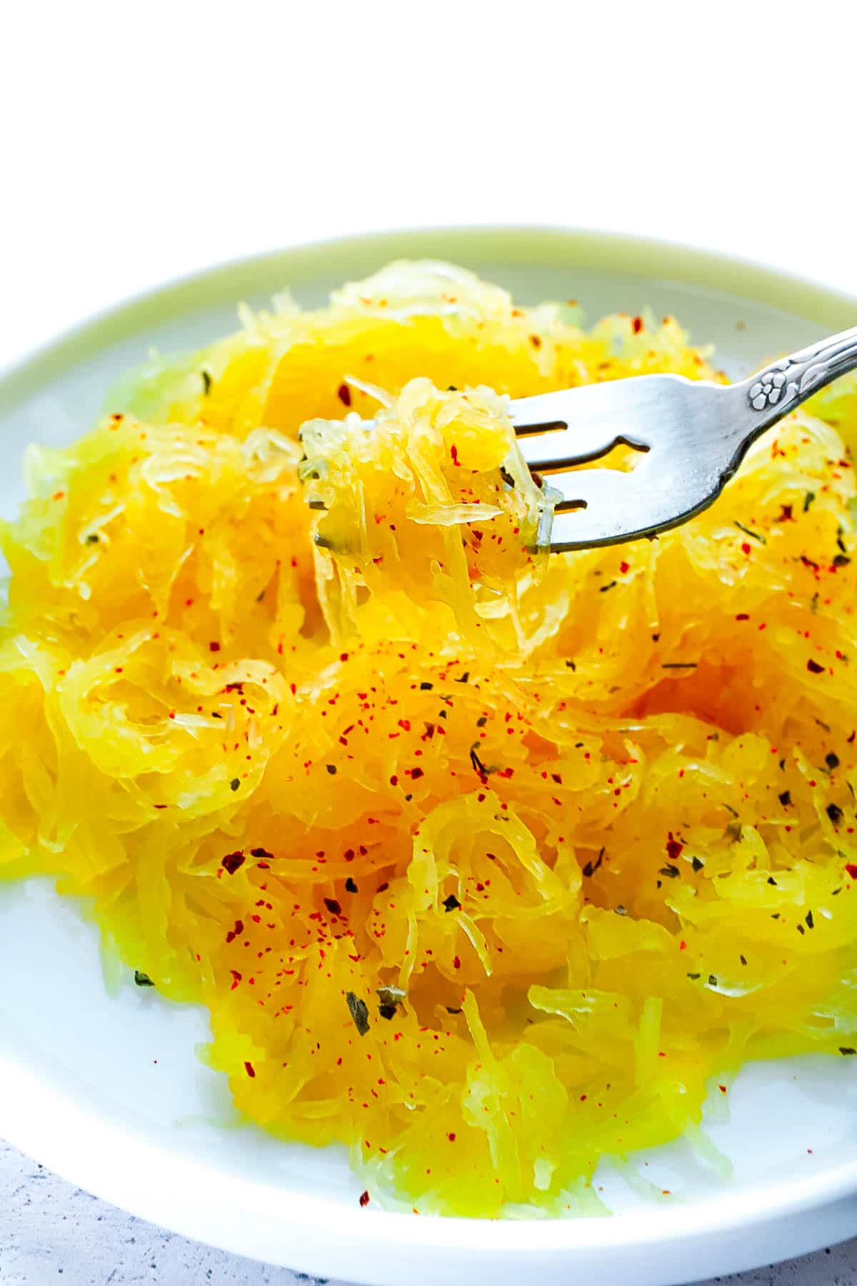 A fork picking up some Spaghetti Squash made in and Instant Pot off of a white plate.