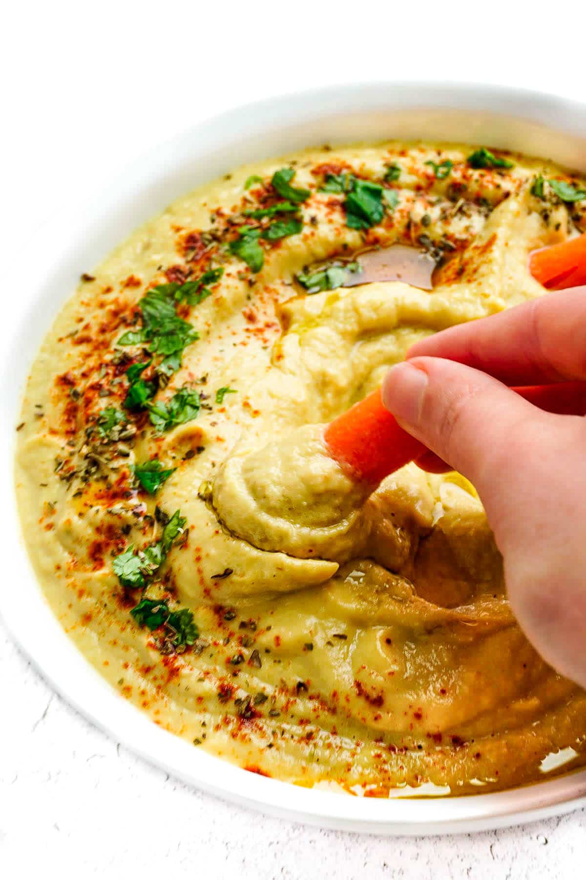 A hand dipping a baby carrot into the Zucchini Hummus.