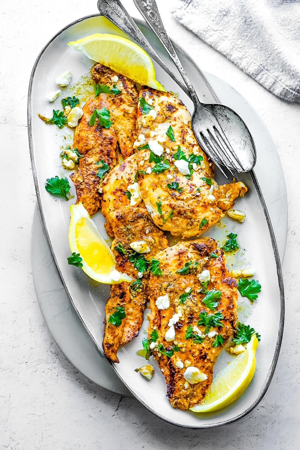 A platter of Greek Lemon Chicken with lemon wedges, feta cheese, and parsley.