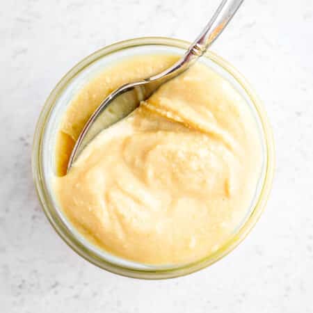 Cashew butter in a glass jar with a spoon in it.