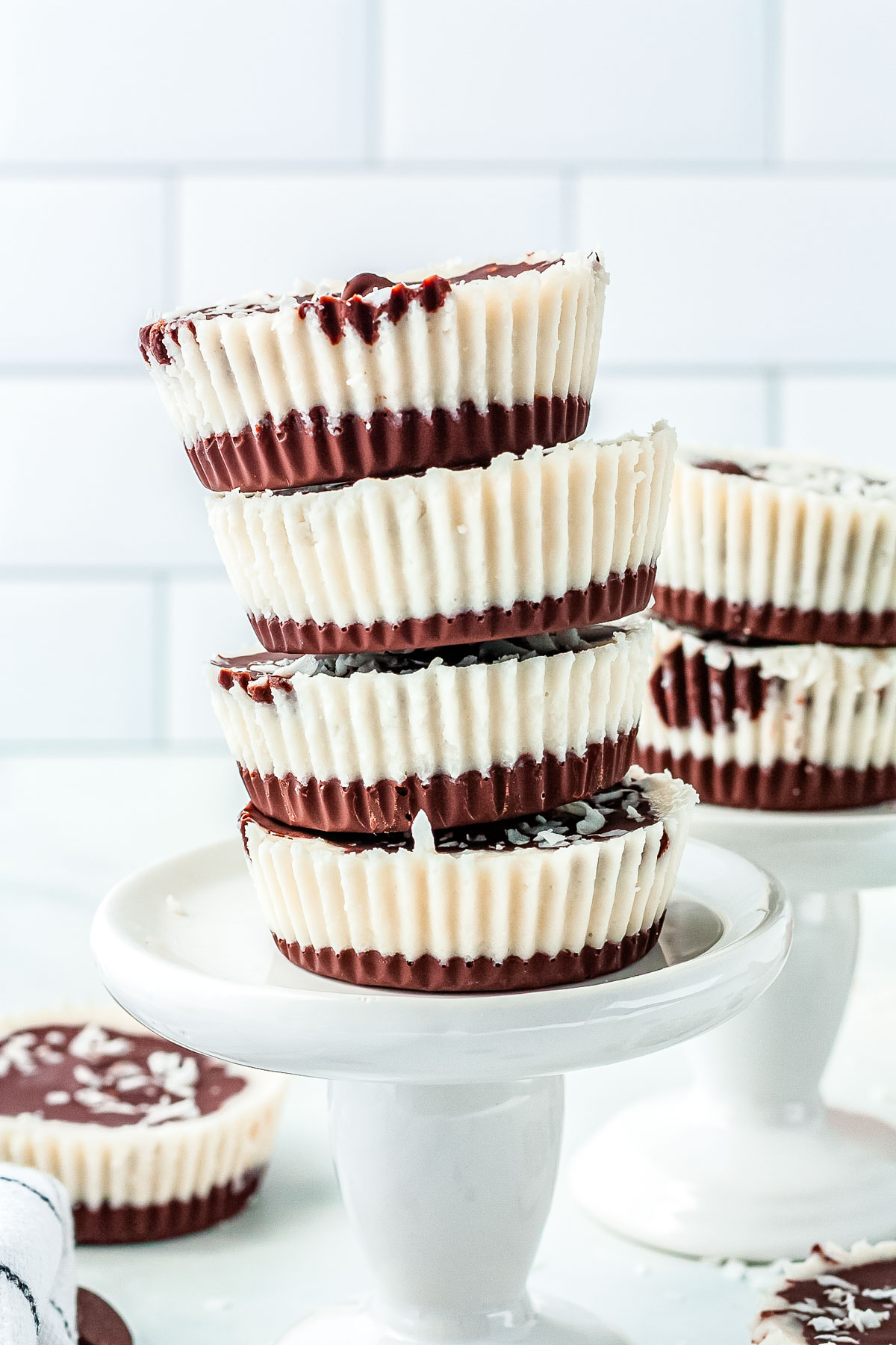 A tall stack of four chocolate coconut butter cups on a white ceramic stand showing the distinct layers of chocolate and creamy coconut filling.