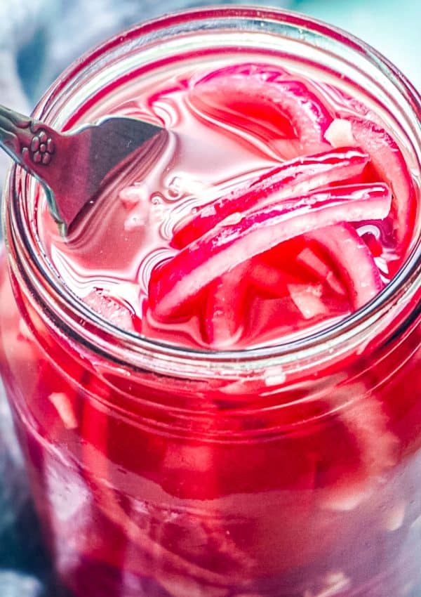 The finished Pickled Red Onions in a jar and a fork fishing some out.