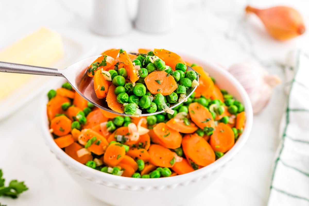 A spoon picking up from carrots and peas.
