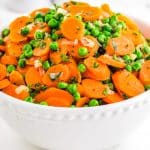 A close up of peas and carrots in a white serving bowl.