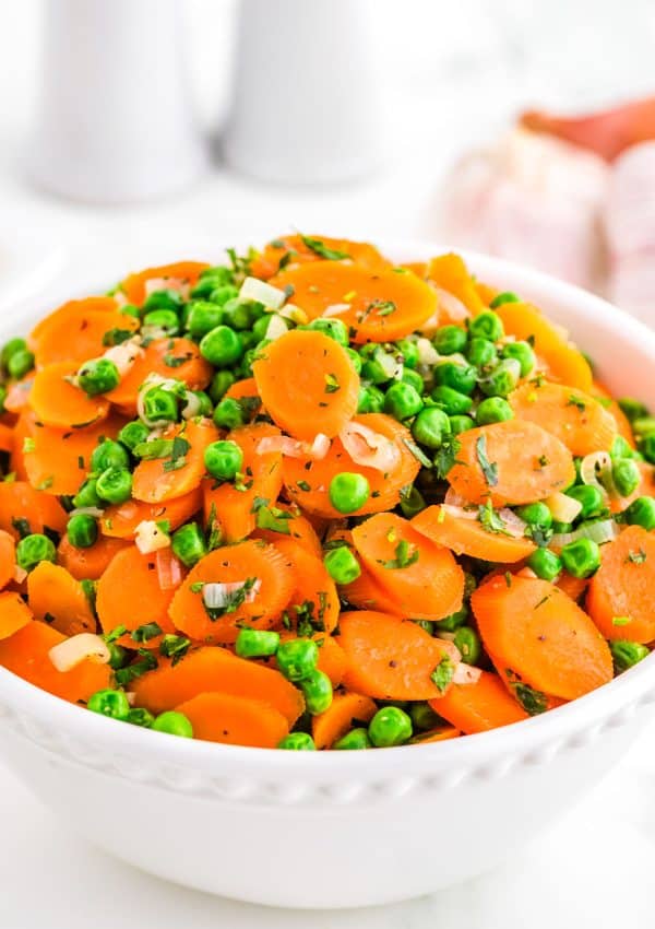 Peas and Carrots in a white serving bowl and garnished with parsley.