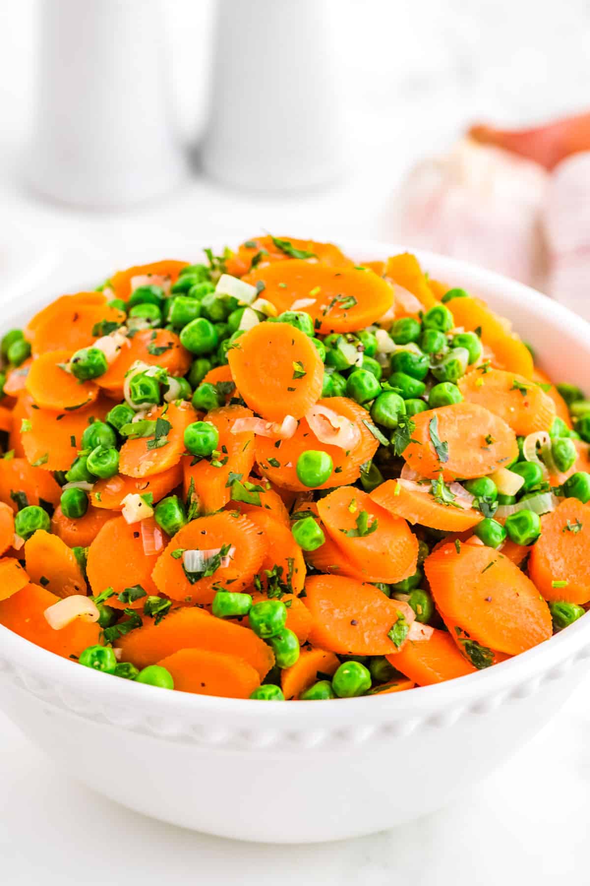Peas and Carrots in a white serving bowl and garnished with parsley. 