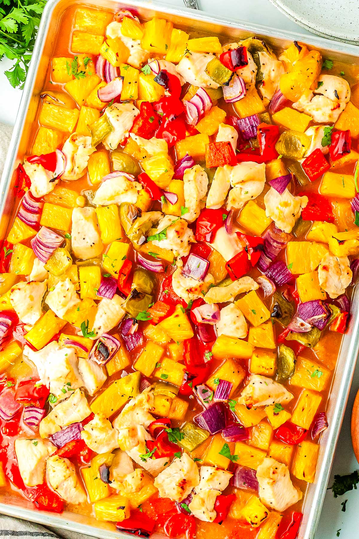 The finished Hawaiian chicken sheet pan meal in the sheet pan and on a counter.
