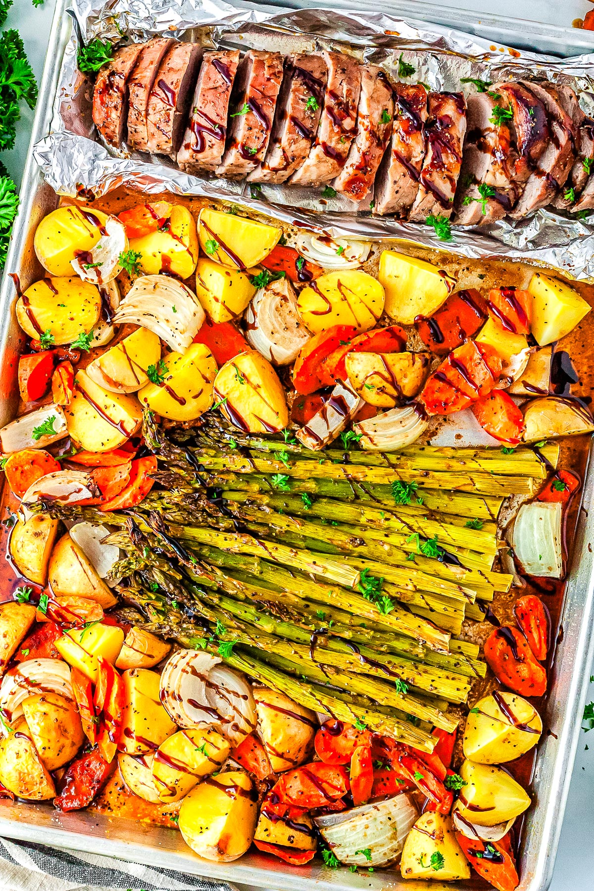 Roast pork tenderlon, potatoes, carrots, onions, and asparagus roasted on a sheet pan.