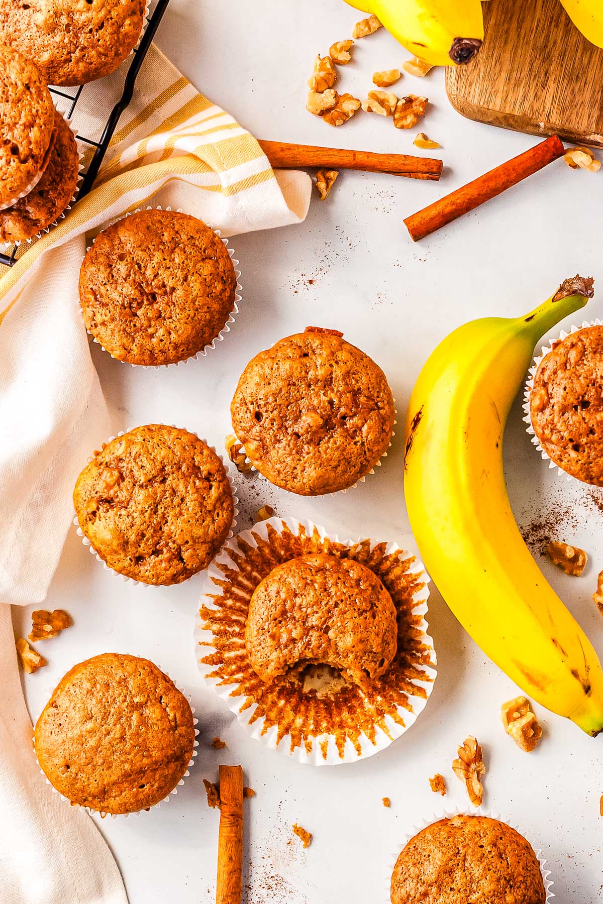 Cottage cheese banana muffins on a counter with a banana, walnuts, and cinnamon sprinkled around them.