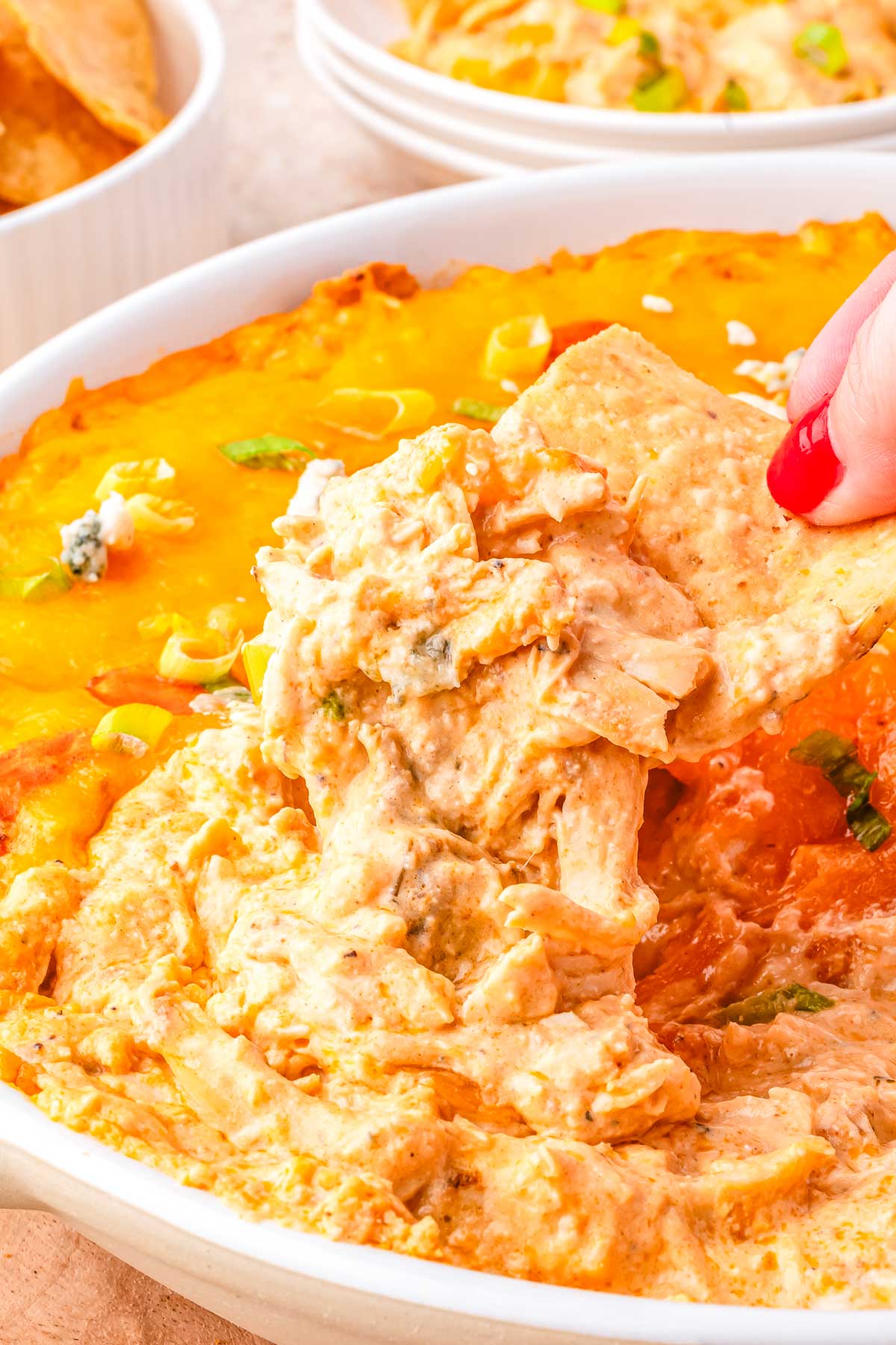 Scooping creamy cottage cheese buffalo chicken dip with a tortilla chip, topped with melted cheddar and green onions.