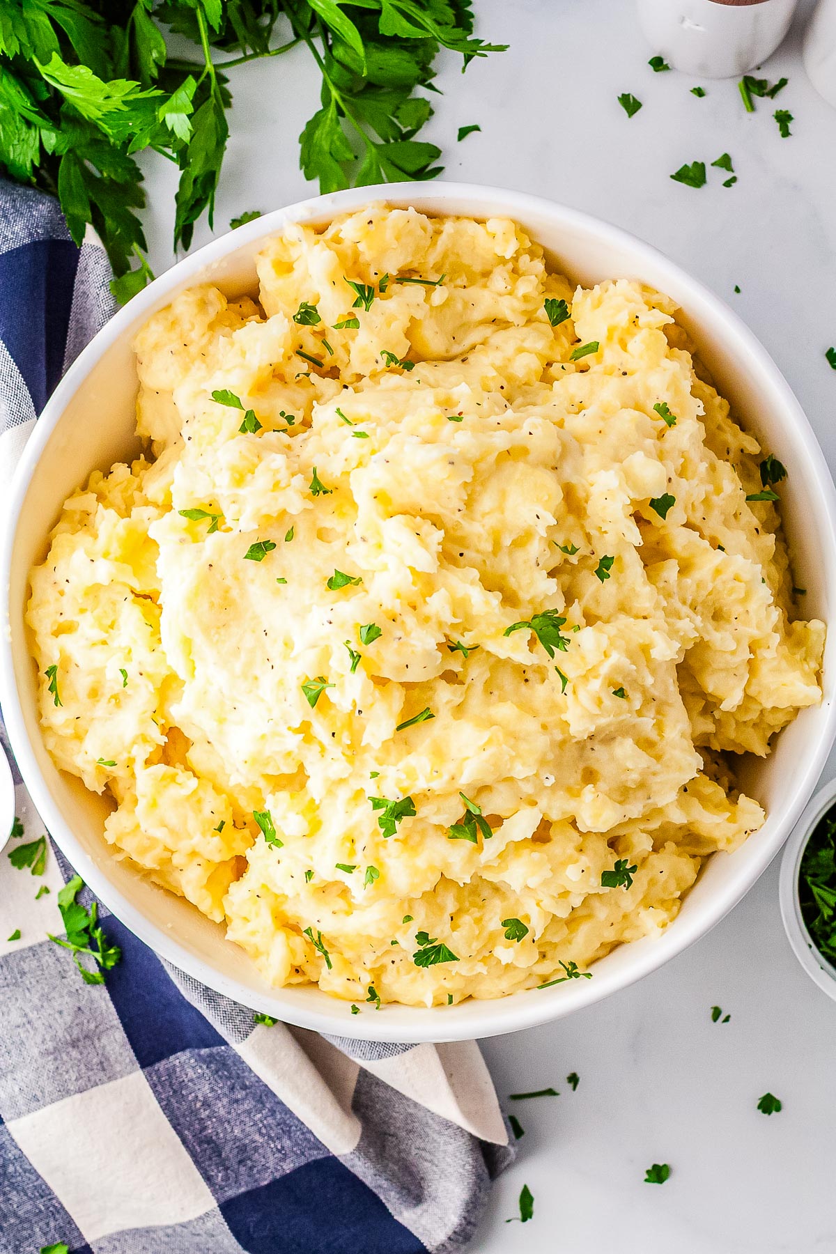 Large bowl of mashed potatoes made with cottage cheese, garnished with fresh parsley and ready to serve on a kitchen counter.