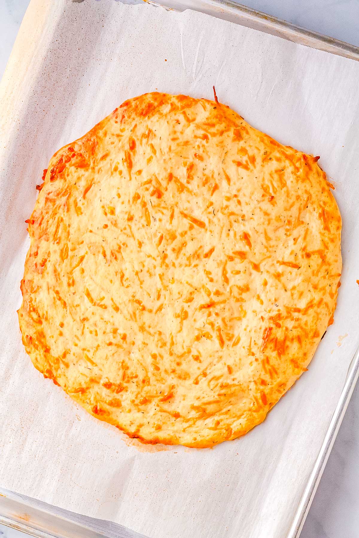 Close-up of freshly baked cottage cheese pizza crust on parchment paper, golden brown and crispy on the edges with melted parmesan throughout.