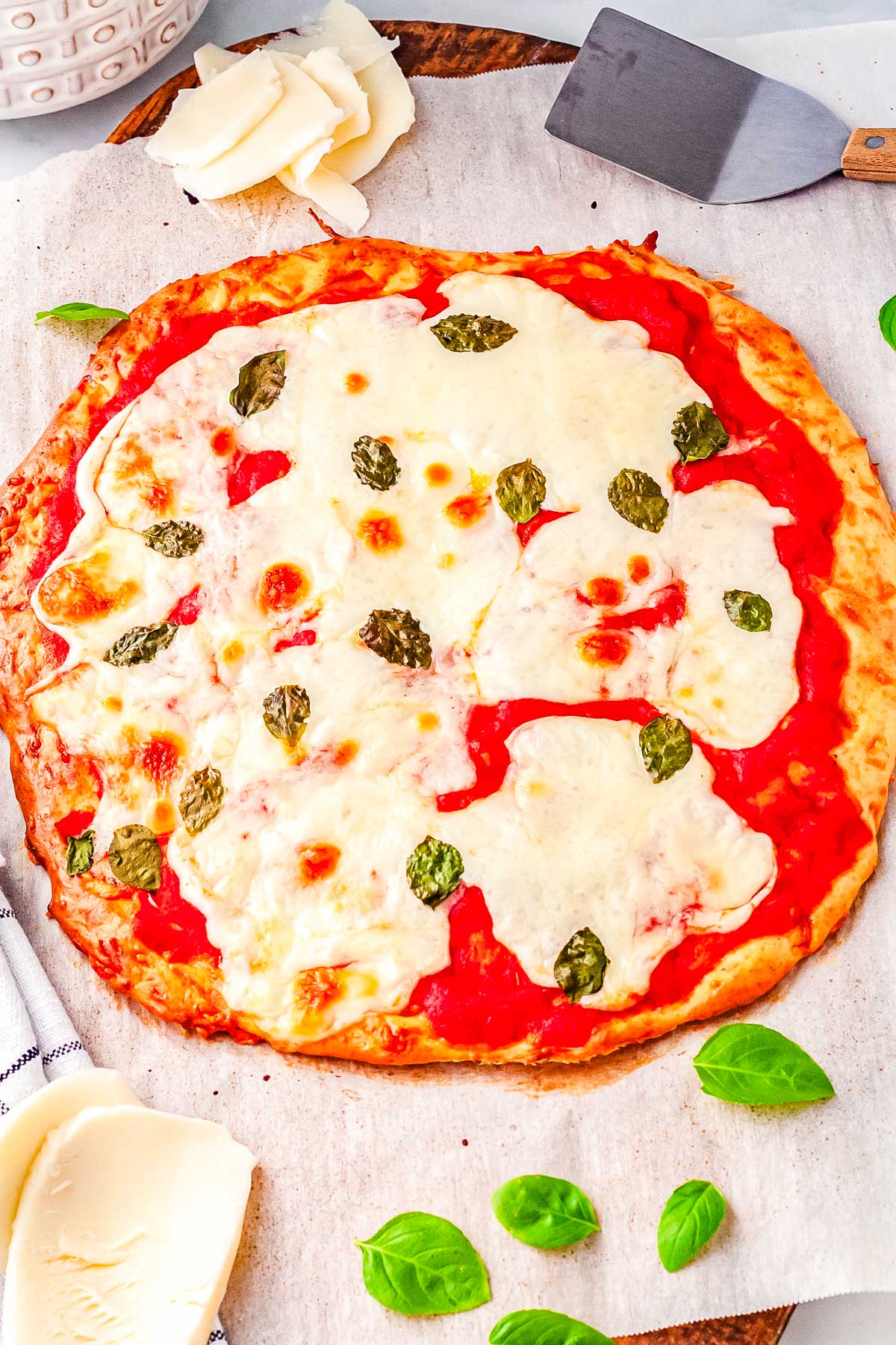 Full cottage cheese pizza baked to golden perfection on parchment, topped with bubbly mozzarella, tomato sauce, and scattered basil leaves, ready to slice and serve.