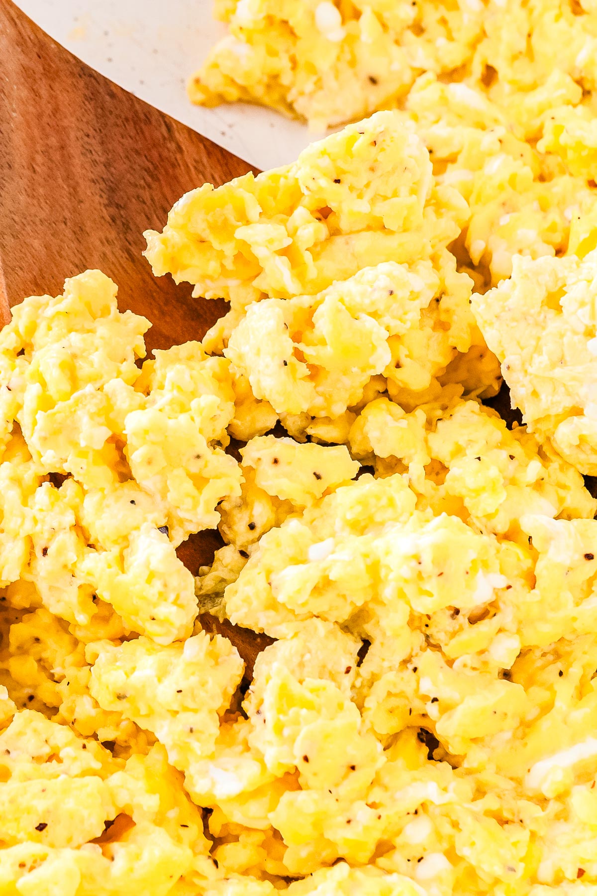 Close up of fluffy cottage cheese scrambled eggs in a skillet with a wooden spatula resting beside them.