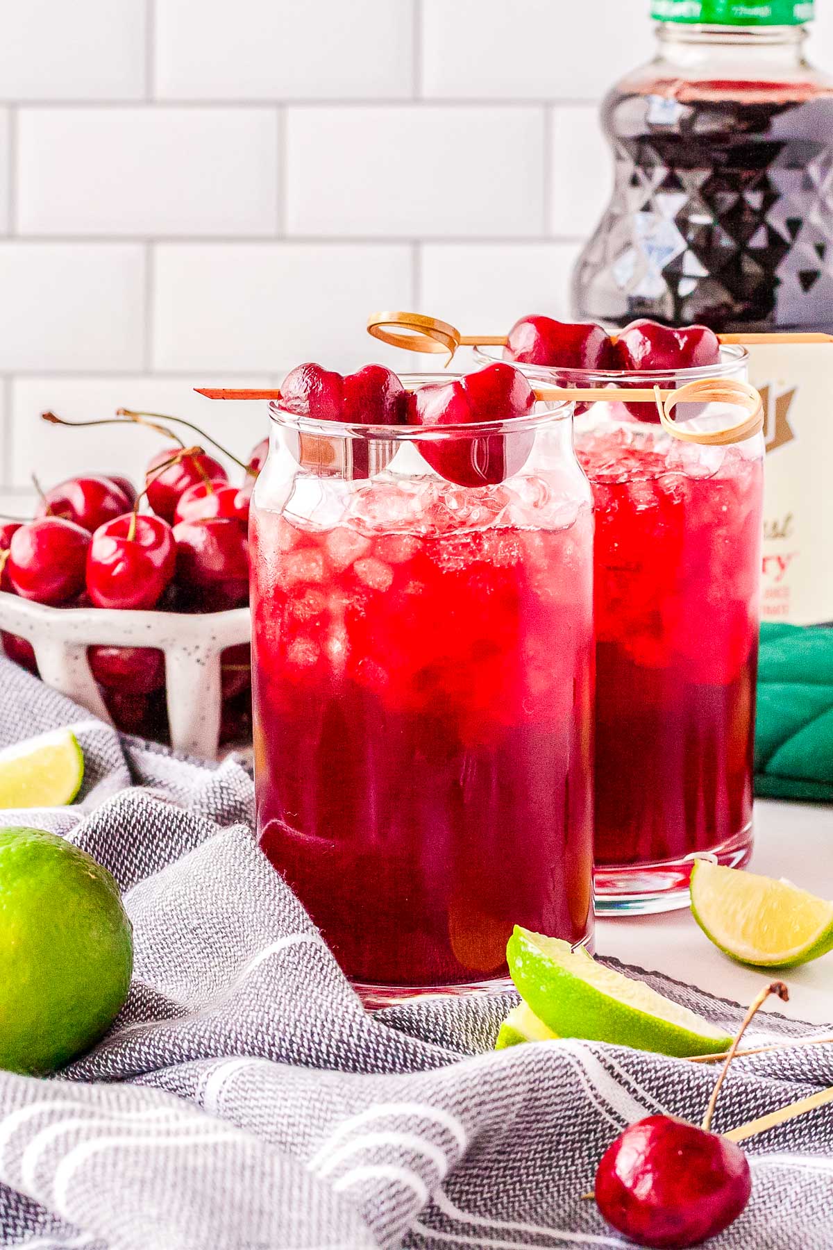 Two glasses of the finished Sleepy Girl Mocktail garnished with lime slices, sitting on a wooden table with a dark, cozy evening background.