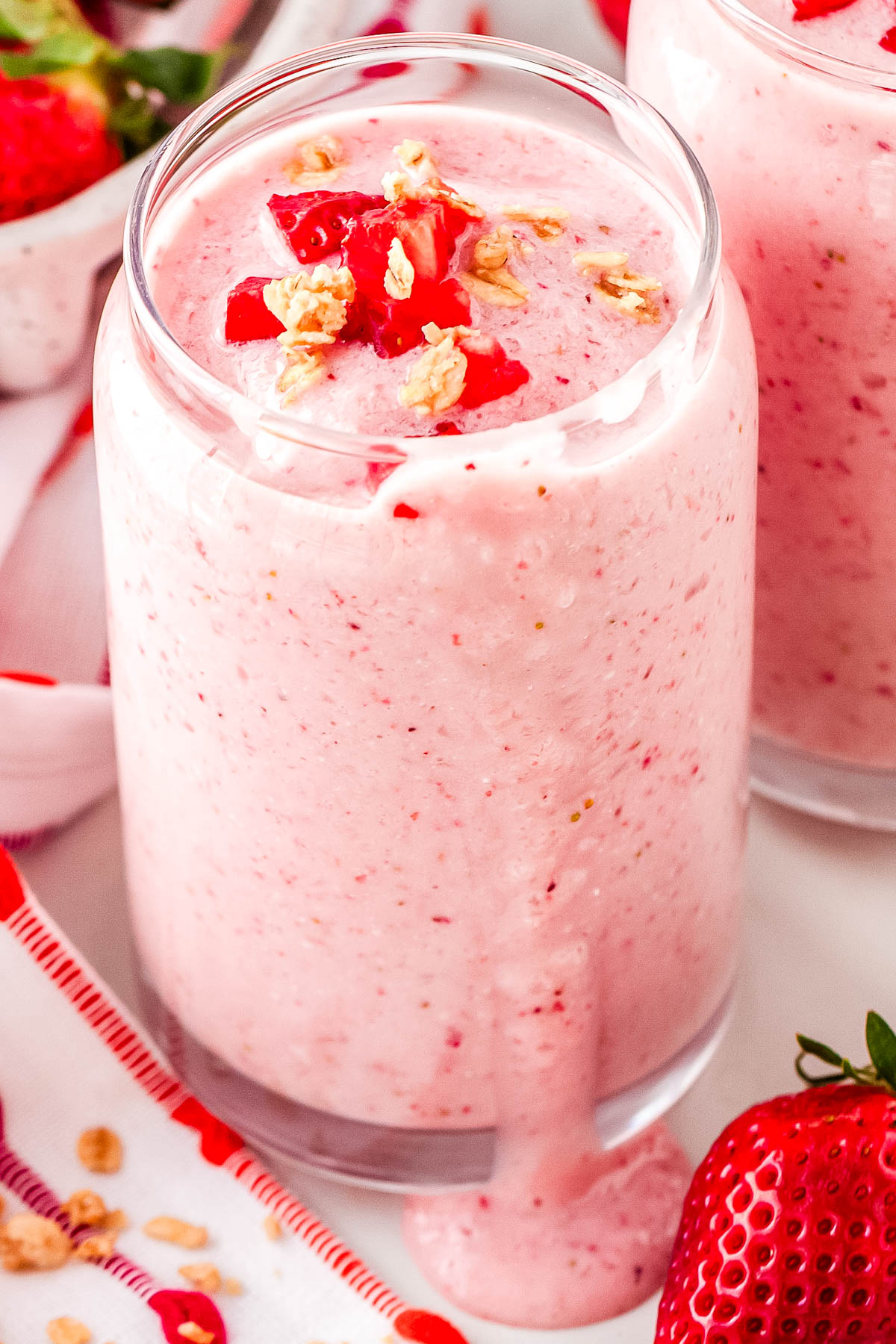 Close up of creamy strawberry cottage cheese smoothie in a glass with granola and fresh strawberry pieces on top.