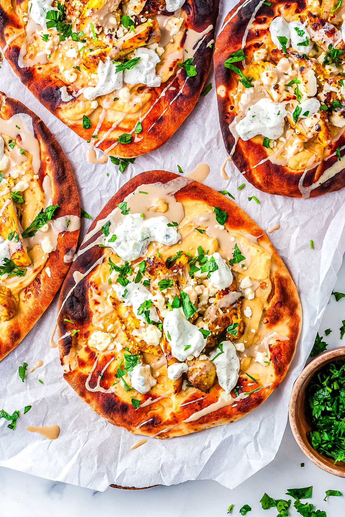 Chicken shawarma flatbread melts with feta, tzatziki, tahini drizzle, and fresh parsley on warm naan.