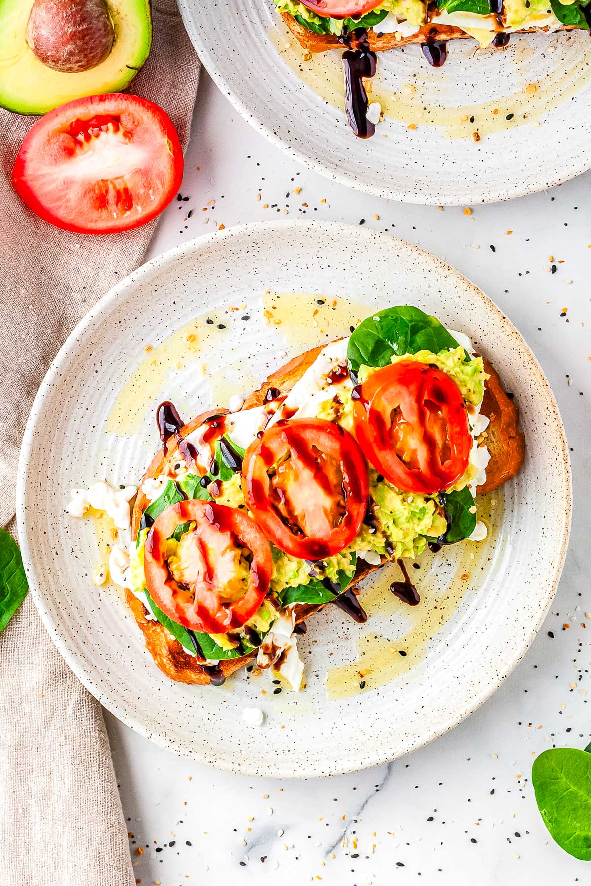 Two plates of cottage cheese avocado toast with spinach, avocado, eggs, tomatoes, and balsamic glaze.
