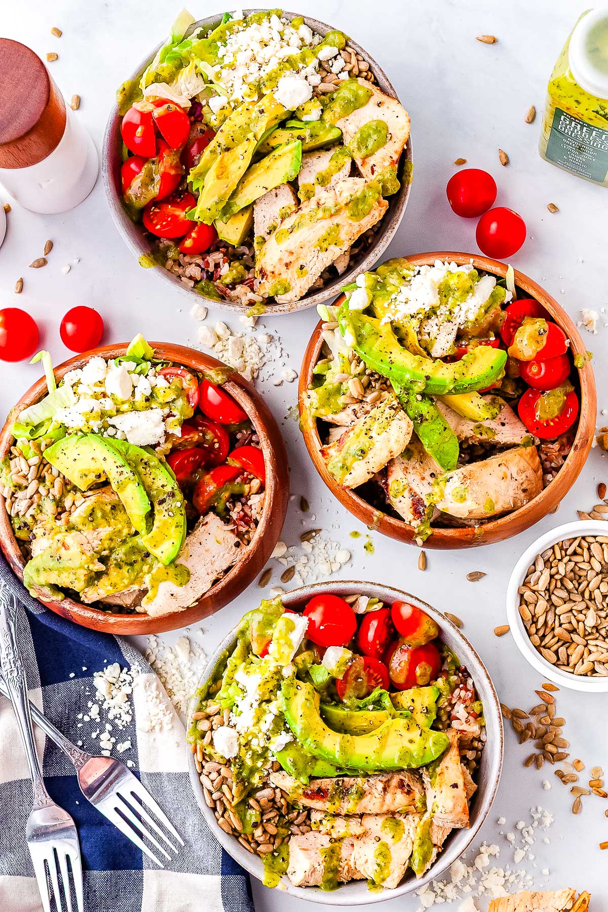 Overhead view of four green goddess chicken power bowls with grains, chicken, avocado, tomatoes, feta, and dressing.
